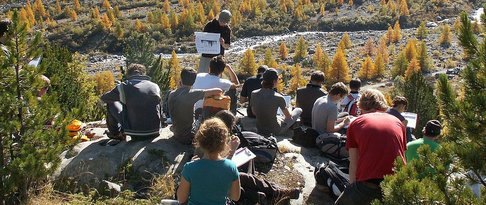 Gruppe sitzt im Wald und hört Rednerin zu